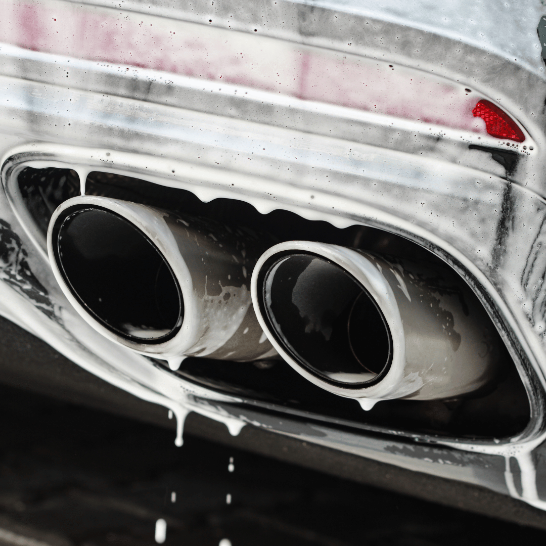 Soap-covered exhaust tips and rear bumper of a car during washing.