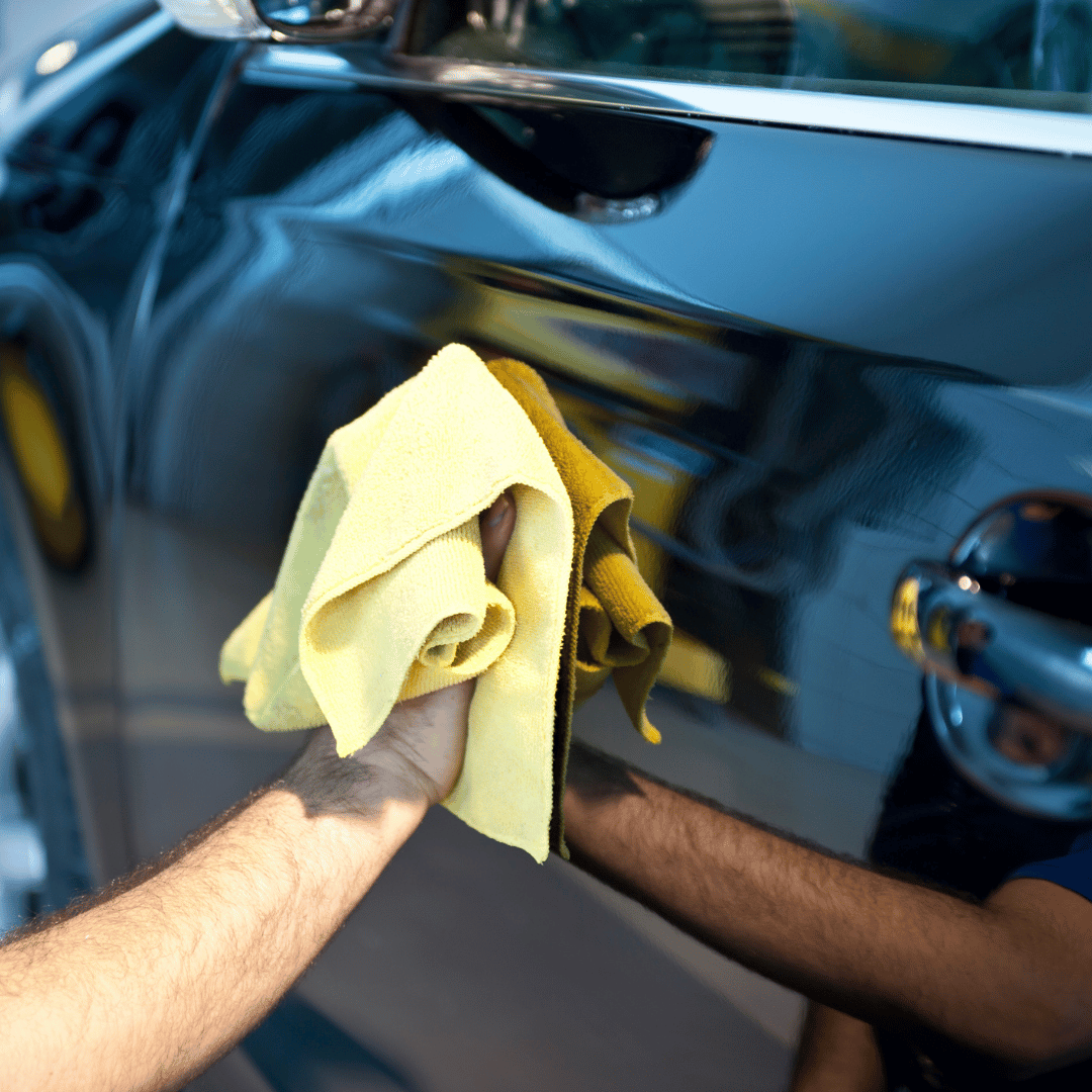 Hands wiping a glossy black car door with a yellow microfiber cloth.