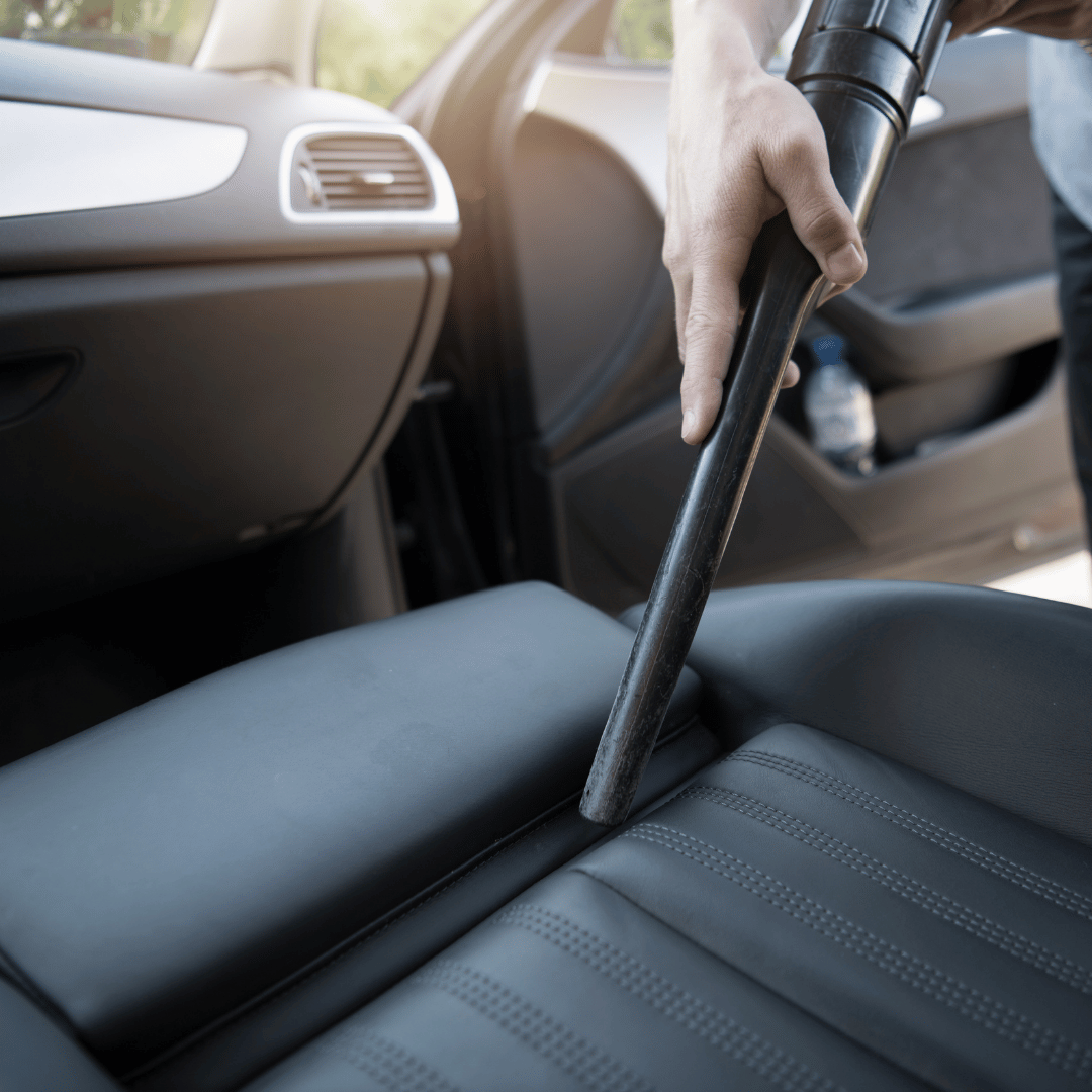 Hand vacuuming a car's front seat through the open door.