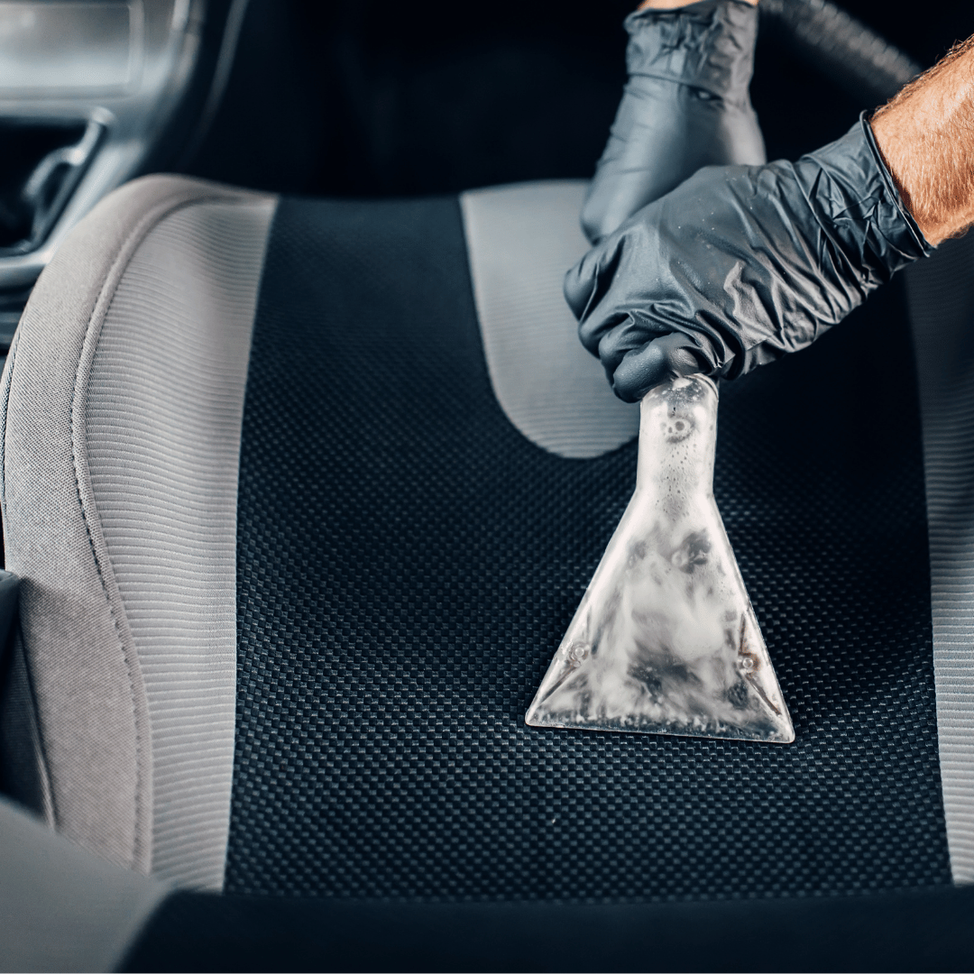 Gloved hand using a wet extraction tool on a car seat with visible foam.