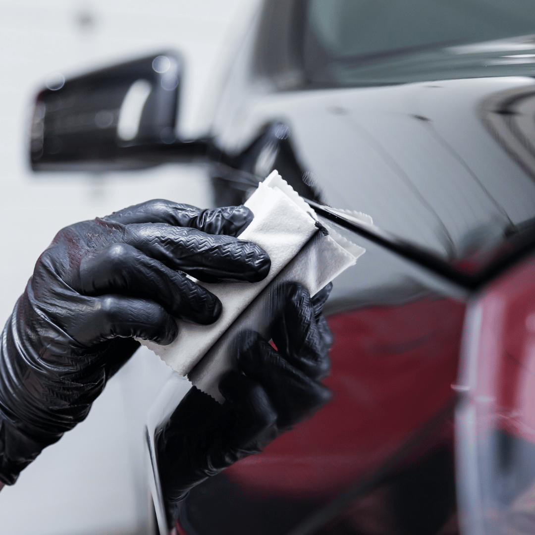 Gloved hand applying coating product to a black car door with a cloth.
